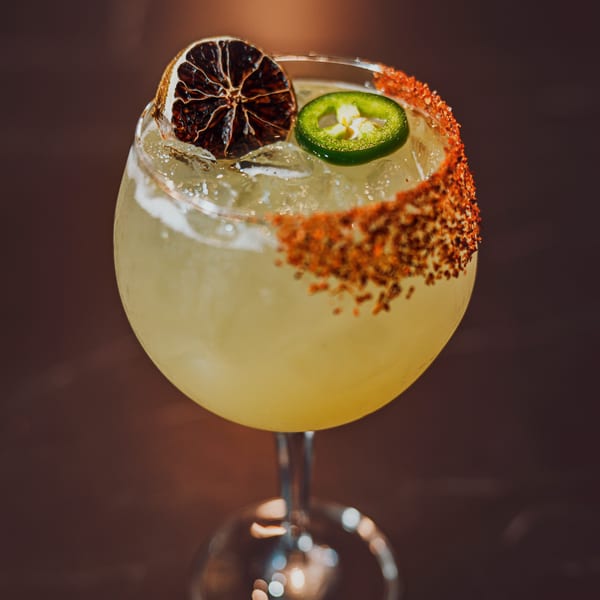 Spicy margarita with a chili-lime rim, garnished with a dried orange slice and jalapeño.